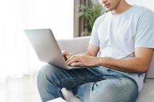 Hombre sentado en el sofá en casa escribiendo en el teclado de la computadora portátil foto