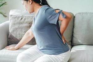 mujer que siente dolor en la espalda sentada en el sofá en casa foto