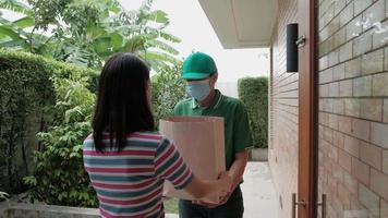 entregador com máscara facial dá um pacote para uma mulher asiática. video