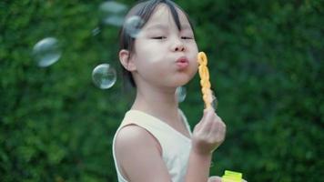 Asian girls playing fun by blowing soap bubbles happily in garden.