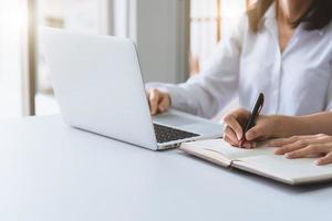 Close up of two businesswoman using laptop and writing on notebook photo