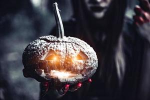 Pumpkin lantern in witch hand. Old woman in dark forest photo