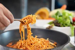 Spaghetti lifted by fork with vegetable salad and dish photo