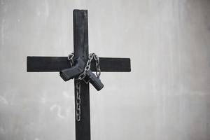 Black cross with chain and handgun on white grunge wall photo
