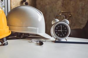 Cerca del reloj y el casco de seguridad de ingeniería en la tabla de planos foto