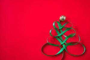 Festive tree made of green ribbon on red background. Christmas concept photo