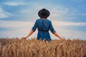 Mujer con vestido y sombrero caminando por campo de trigo