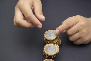 Manos de niño poniendo monedas de oro y plata en la pila de monedas