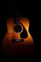 Acoustic guitar on a black background between light or shadows photo