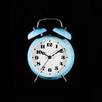 Reloj despertador de mesa clásico azul claro sobre fondo negro foto