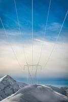 Pylons covered with snow in the high mountains carry energy downstream photo