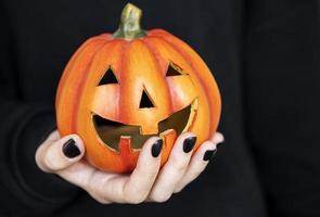 Female hands holding funny pumpkins on black background photo