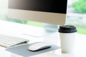 Close up of disposable coffee cup and computer photo