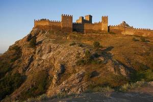 Fortaleza de pie en lo alto de una montaña al amanecer. foto