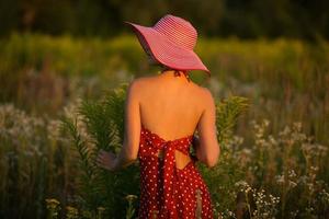 Elegant woman in a hat among wildflowers at sunset photo