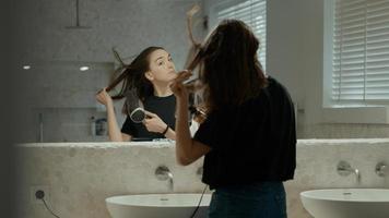 Mujer con secador de pelo en el baño mirando en el espejo