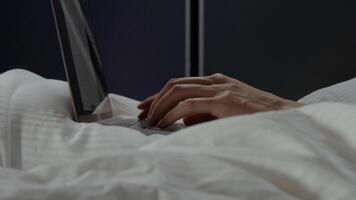 Fingers of man typing on laptop on bed photo