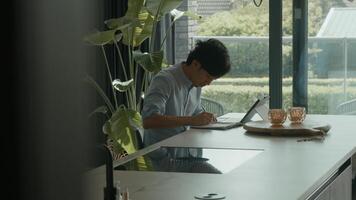 El hombre en la cocina mira fijamente y escribe en un cuaderno foto