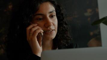 Woman sits with laptop whilst calling and drinking photo