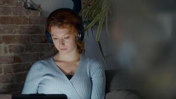 Joven mujer blanca en la sala de estar, auriculares en los oídos, viendo la tableta foto