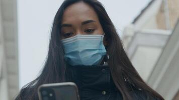 Head shot of young mixed race woman with face mask looking at phone photo