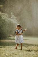 Cute little girl having fun under irrigation sprinkler photo