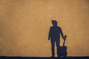 La sombra y la silueta del hombre con una guitarra de fondo de muro de hormigón foto