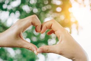 La mano de la mujer hace forma de corazón en la naturaleza verde del bokeh. foto