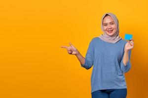 Smiling Asian woman holding credit card and pointing finger photo