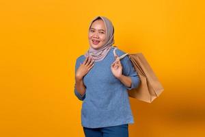 Surprised Asian woman holding shopping bag over yellow background