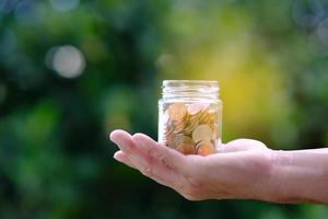 Saving money concept, hand holding coin in jar photo