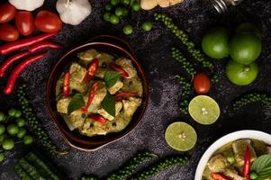 Pork green curry in a brown bowl with spices on a black cement photo