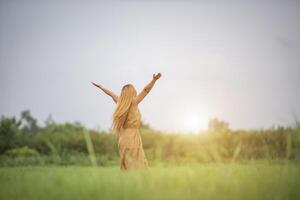 Young woman standing in grass field raising hands in the air. photo