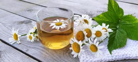 Chamomile aromatic tea in a glass cup on a wooden background