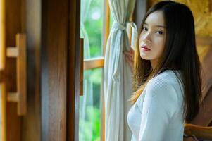 A woman is standing by a window looking out photo