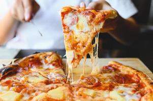 rebanada de pizza con queso de leña en la mano. pizza hawaiana y salami foto
