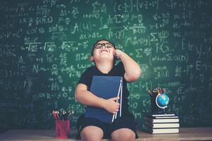 niño pensativo con libro cerca de una junta escolar foto