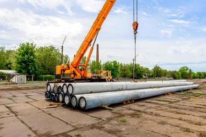 Unloading of concrete high-voltage poles at the construction site using a lifting crane photo