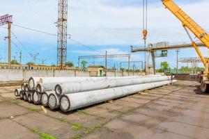 Unloading of concrete high-voltage poles at the construction site using a lifting crane photo