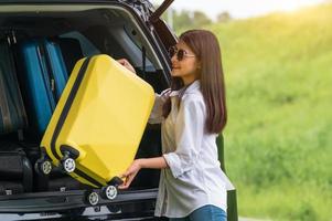 Asian woman lifting yellow suitcase into SUV car during travel photo