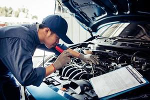 Car mechanic technician holding flashlight checking engine photo