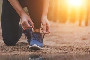 Joven mujer corriendo fitness atar cordones de los zapatos al aire libre en el bosque