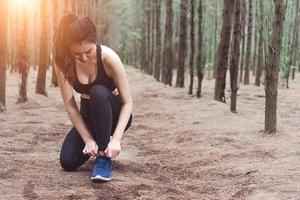 Mujer atando los cordones de los zapatos al trotar en el bosque atrás foto