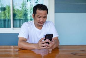 Asian man wearing white shirt using the phone on a wooden table photo