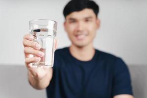 Hombre asiático bebiendo un vaso de agua en el sofá del salón foto