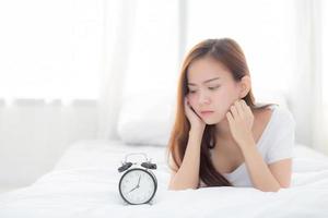 Young asian woman wake up in morning annoyed looking  alarm clock. photo