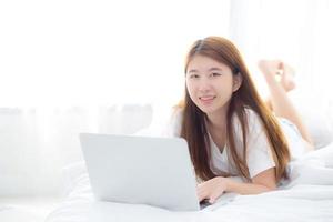 joven asiática acostada en la cama con ordenador portátil. foto