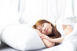 joven asiática dormir acostado en la cama con la cabeza apoyada en la almohada. foto