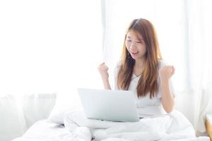 Young asian woman using laptop work with success on bed. photo