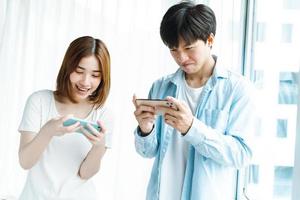 Young Asian couple playing games together on mobile phones photo